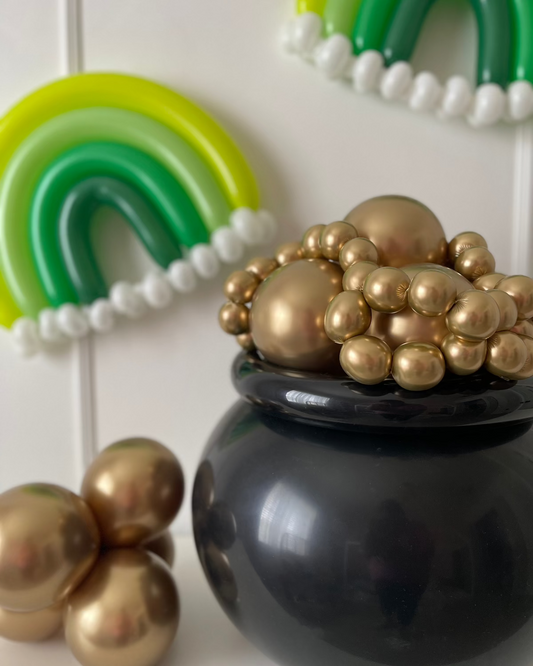 A black balloon pot filled with gold balloons, styled next to green monochrome balloon rainbows with white cloud details. This festive setup is part of the “You’re My Lucky Charm Balloon Class” by Lilly Jimenez, perfect for St. Patrick’s Day decor, displays, or photoshoots.