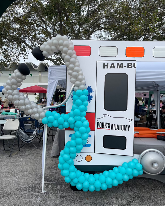 Large balloon stethoscope decor attached to an ambulance backdrop, designed for a medical-themed outdoor event. This eye-catching piece is ideal for hospital events, doctor celebrations, and health awareness setups. Part of Lilly’s Balloon Stethoscope Tutorial.