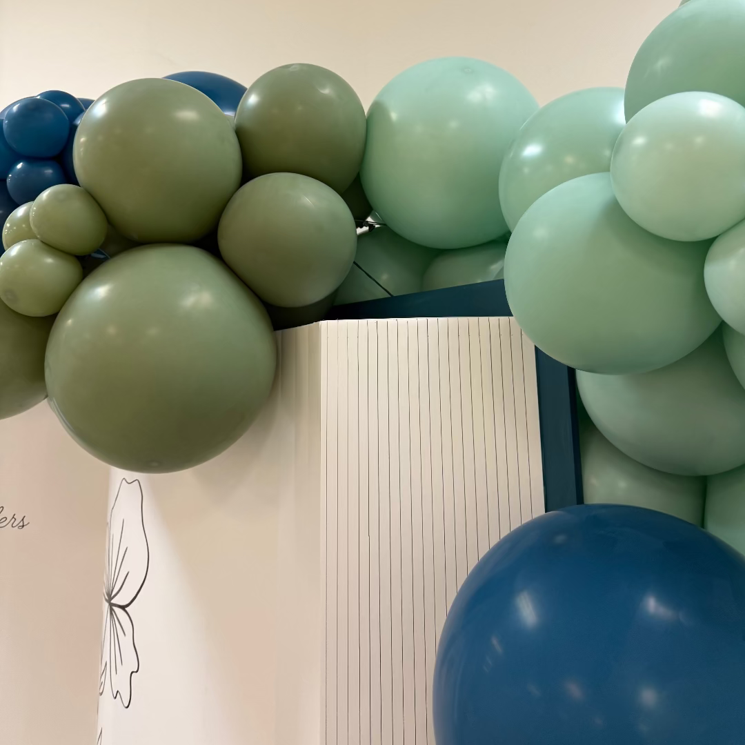 Close-up of an oversized open book backdrop with a green and blue balloon garland cascading across the top. The foamboard book features printed page lines and floral illustrations, making it a versatile and customizable backdrop for storybook events, graduations, weddings, and photo booths. Ideal for balloon stylists and event decorators using the digital download template.