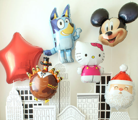 DIY Macy’s Thanksgiving Day Parade-inspired backdrop featuring foamboard NYC skyline cutouts, foil balloons (Bluey, Mickey, Hello Kitty, Turkey), and festive oversized confetti for family photo shoots.