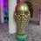 Giant gold balloon soccer trophy sculpture with green balloon base displayed indoors at a FIFA World Cup event venue.