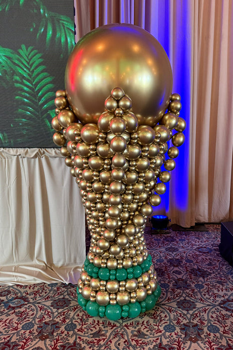 Close-up of a giant gold balloon soccer trophy sculpture with green balloon base at a FIFA World Cup event setup.