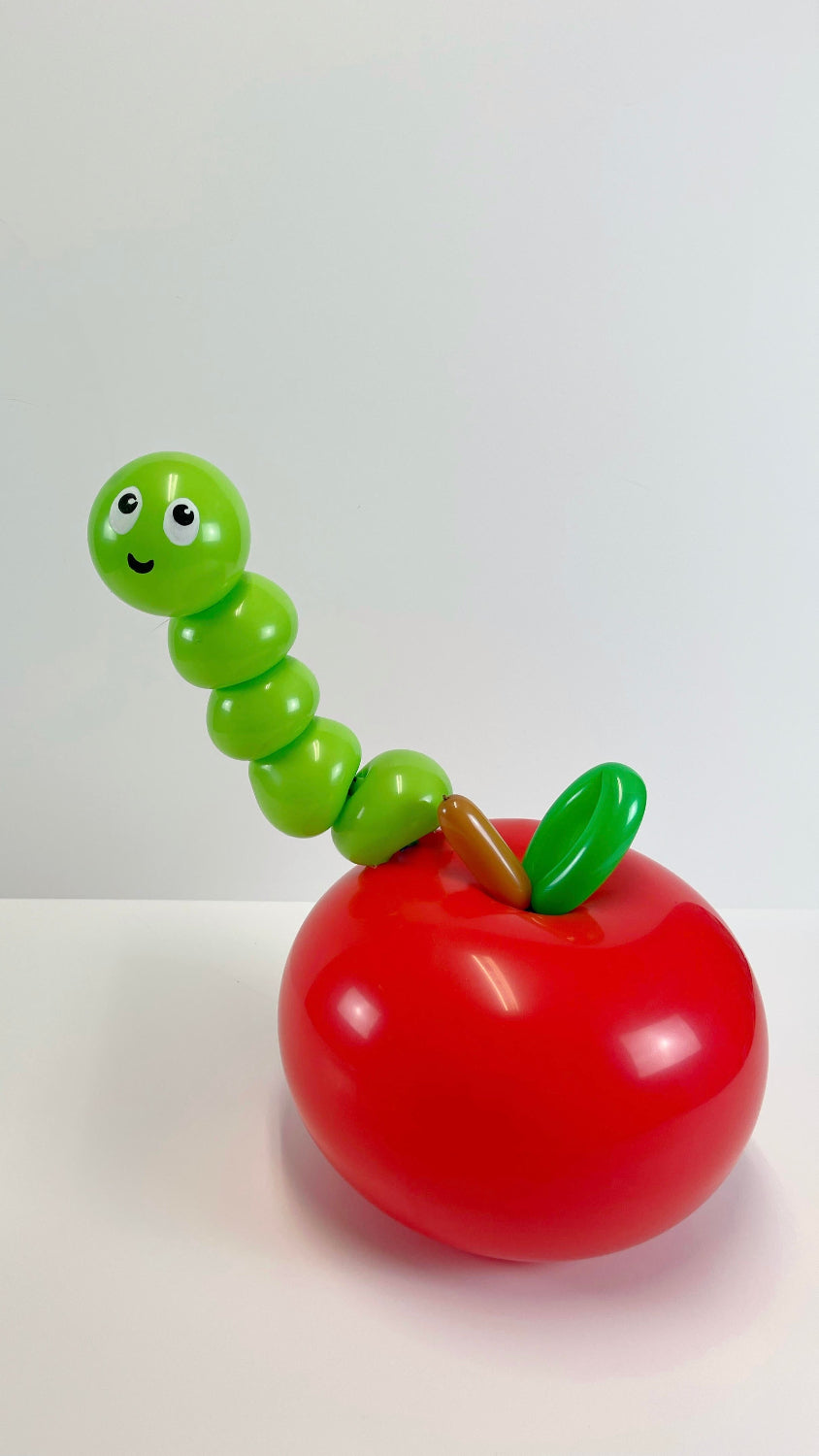 Adorable red apple balloon with a smiling green balloon worm peeking out, perfect for back-to-school balloon decorations, teacher appreciation gifts, and classroom centerpieces. This fun and whimsical design adds a playful touch to any school-themed event and is a great project for balloon artists looking to create cute and memorable balloon sculptures.