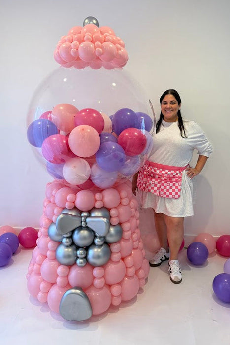 Lilly standing next to a 7 foot balloon gumball machine made with linking balloons in pink, purple, and silver for birthday party decor and large event installs.