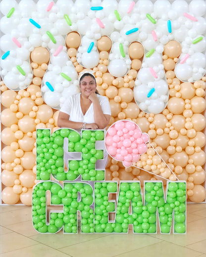 Lilly Jimenez poses in front of a giant Balloon Mosaic® Ice Cream backdrop featuring a peach and white balloon drip wall with colorful sprinkle accents. The oversized “ICE CREAM” sign is filled with green and pink balloons, making this sweet setup perfect for summer parties, dessert bars, or photo ops.