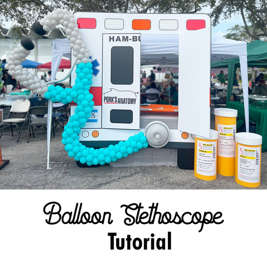Oversized balloon stethoscope displayed on a faux ambulance backdrop at an outdoor event. Perfect for hospital celebrations, doctor-themed parties, and health-related decor. Learn how to create this fun balloon sculpture in the Balloon Stethoscope Tutorial by Lilly.