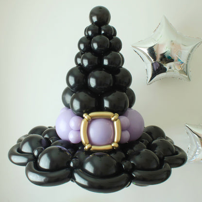 A black balloon witch hat crafted with stacked balloon layers, featuring a gold buckle and purple accents at the base. Silver star balloons float in the background, adding a magical touch. This whimsical Halloween decoration is perfect for spooky parties, themed events, and festive displays. Learn how to create this eye-catching piece in the Witch Hat Balloon Tutorial!







