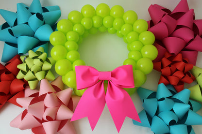 Vibrant green balloon wreath surrounded by large colorful paper gift bows in teal, red, pink, blush, and lime. This festive flat lay showcases creative Christmas decor perfect for holiday parties, DIY lovers, and eye-catching seasonal displays.