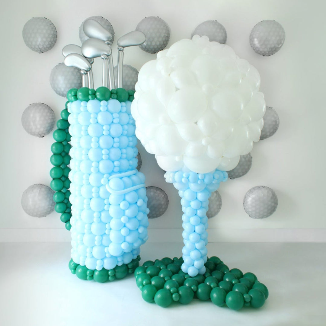 Golf Balloon Class display featuring a balloon golf bag with silver balloon clubs and a giant golf ball on a tee. This oversized balloon structure is taught in 2 video lessons and is perfect for golf tournaments, birthdays, baby showers, retirements, Father’s Day, country club events, corporate parties, and store openings. A standout golf balloon décor idea that can also be customized with logos for branded celebrations.