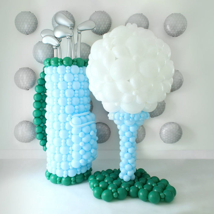 Golf Balloon Class display featuring a balloon golf bag with silver balloon clubs and a giant golf ball on a tee. This oversized balloon structure is taught in 2 video lessons and is perfect for golf tournaments, birthdays, baby showers, retirements, Father’s Day, country club events, corporate parties, and store openings. A standout golf balloon décor idea that can also be customized with logos for branded celebrations.