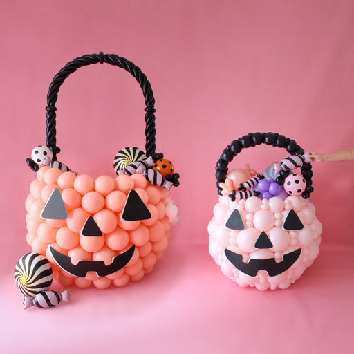 Balloon pumpkin treat buckets made from orange and white balloons with black jack-o-lantern faces, twisted balloon handles, and balloon candy accents. Perfect DIY Halloween balloon décor for parties, events, and festive photo backdrops.