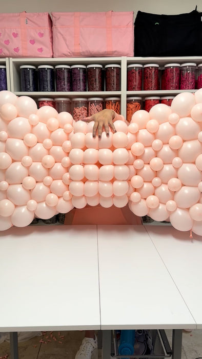 Close-up of the blush pink linking balloon bow center section on a table, showing the tight bubble grid technique and structural core students learn to build in the Linking Balloon Bows Class.