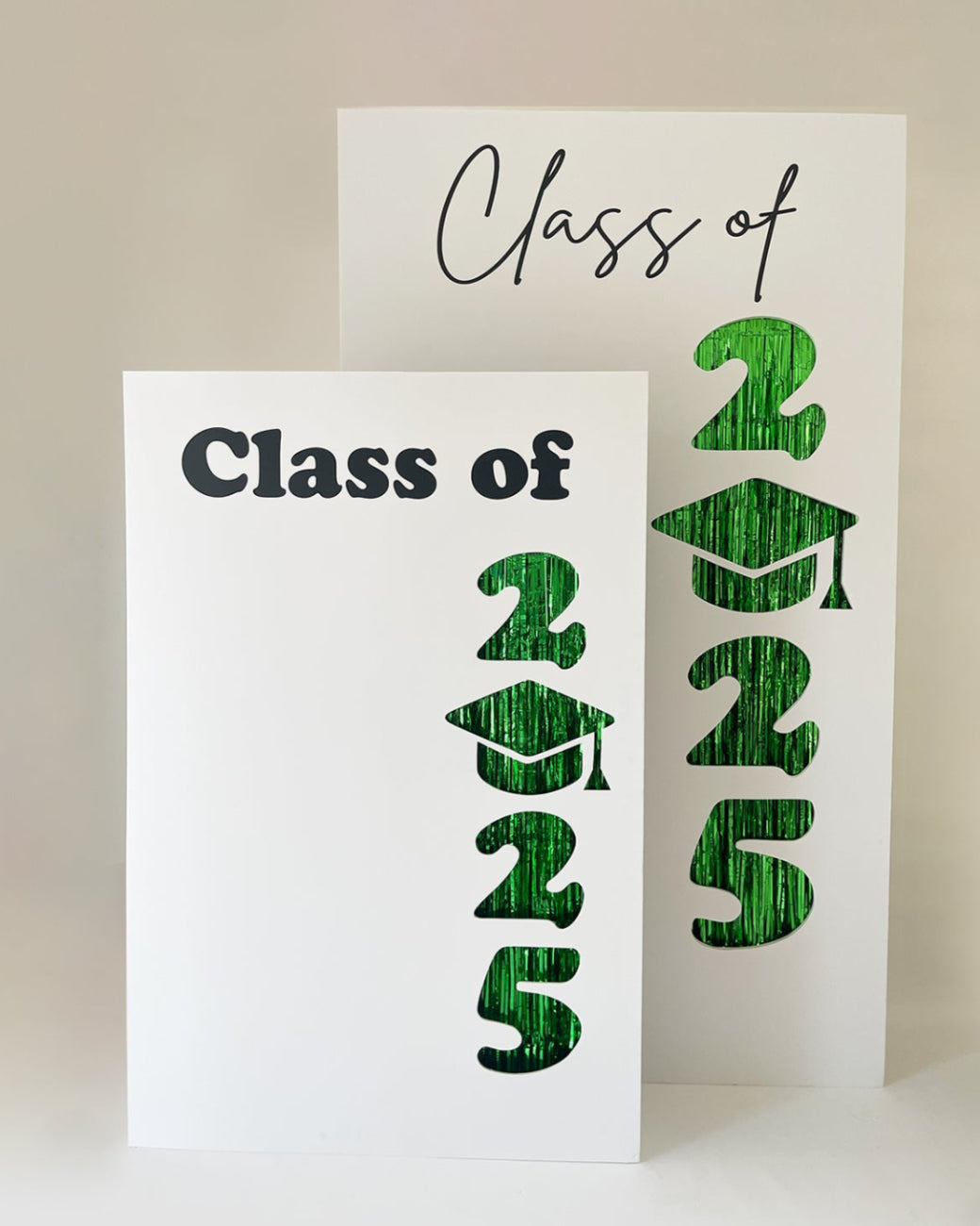Two foam board graduation backdrops featuring “Class of 2025” with cut-out numbers and a graduation cap replacing the zero. Green foil fringe peeks through the cutouts. Includes two font styles for “Class of” and comes in two sizes—ideal for preschool, elementary, middle school, high school, and college graduation photo backdrops.