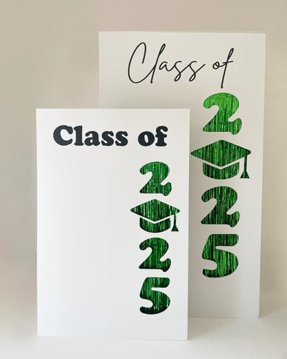 Two foam board graduation backdrops featuring “Class of 2025” with cut-out numbers and a graduation cap replacing the zero. Green foil fringe peeks through the cutouts. Includes two font styles for “Class of” and comes in two sizes—ideal for preschool, elementary, middle school, high school, and college graduation photo backdrops.