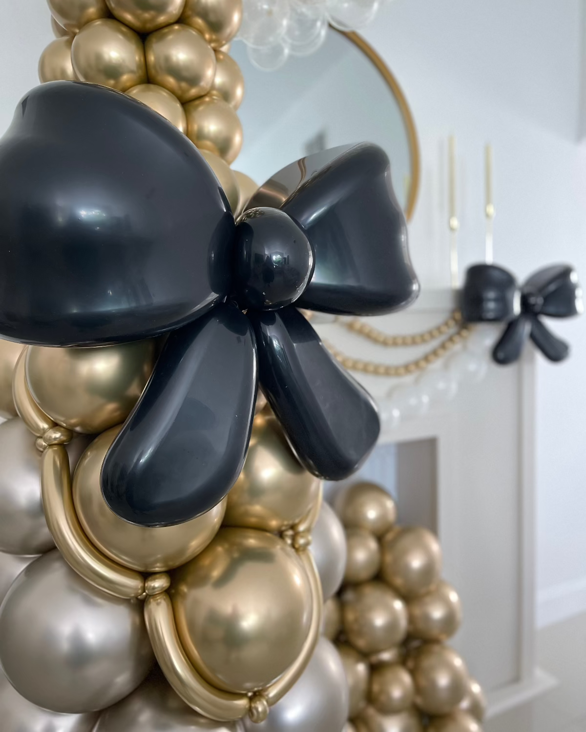 Close-up view of a shiny black balloon bow on a gold and pearl balloon champagne bottle, designed by Lilly Jimenez. Elegant and oversized, this party decor piece is perfect for weddings, cocktail hours, or New Year's Eve displays. Balloon bow detail highlights the luxurious finish.