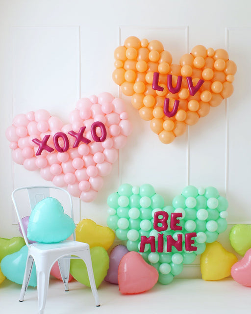 Balloon heart wall decorations inspired by conversation hearts, featuring pastel-colored balloons with phrases "XOXO," "LUV U," and "BE MINE."