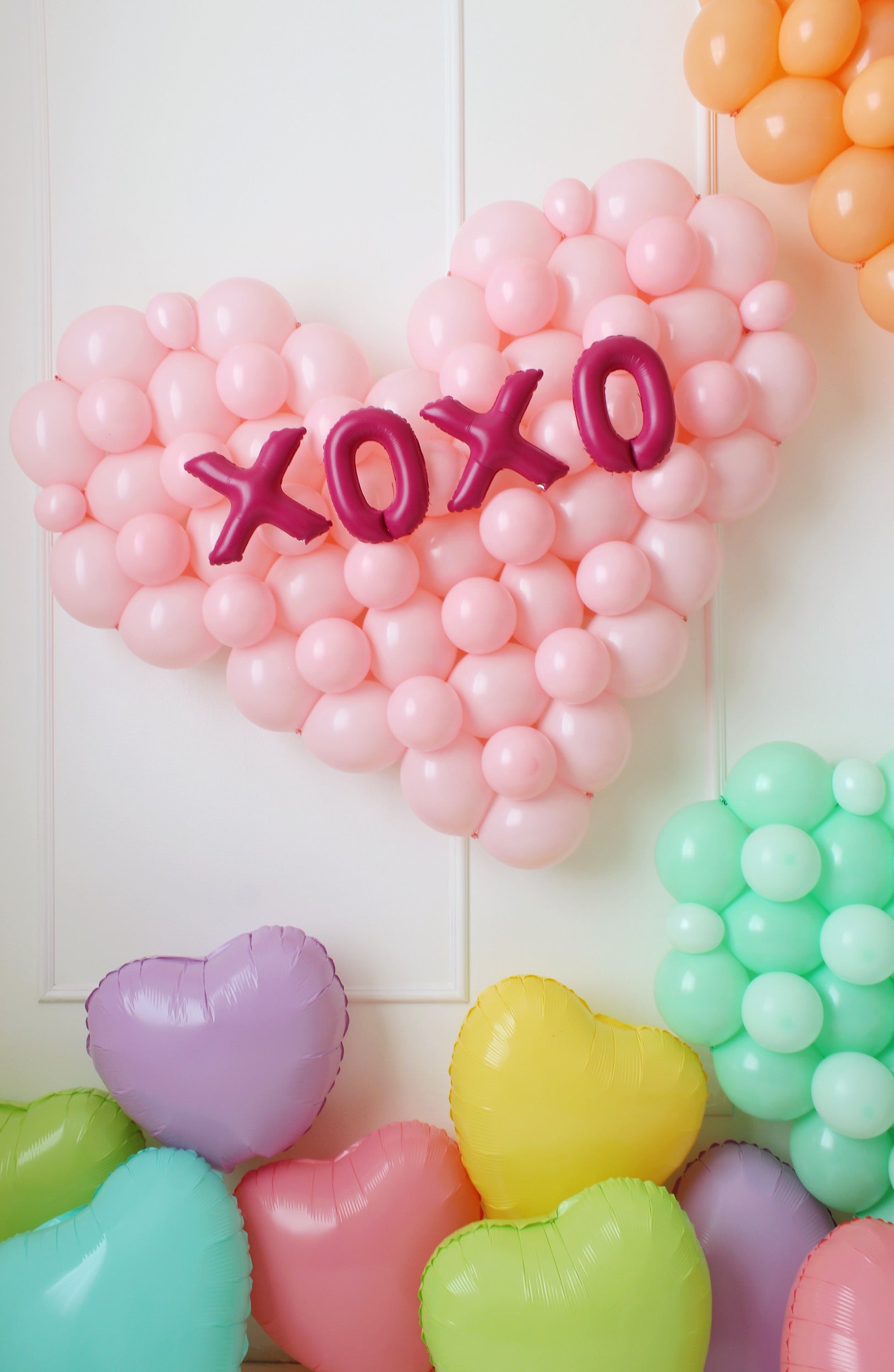 Balloon heart wall decorations inspired by conversation hearts, featuring pastel-colored balloons with phrase "XOXO" 