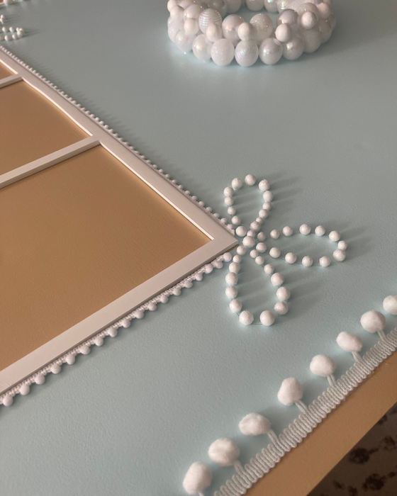 Close-up of a pastel blue oversized gingerbread house backdrop showing delicate candy-style details, including pearl bead wreath, white pom pom trim, and decorative bow accents, perfect for Christmas displays and festive photo setups.