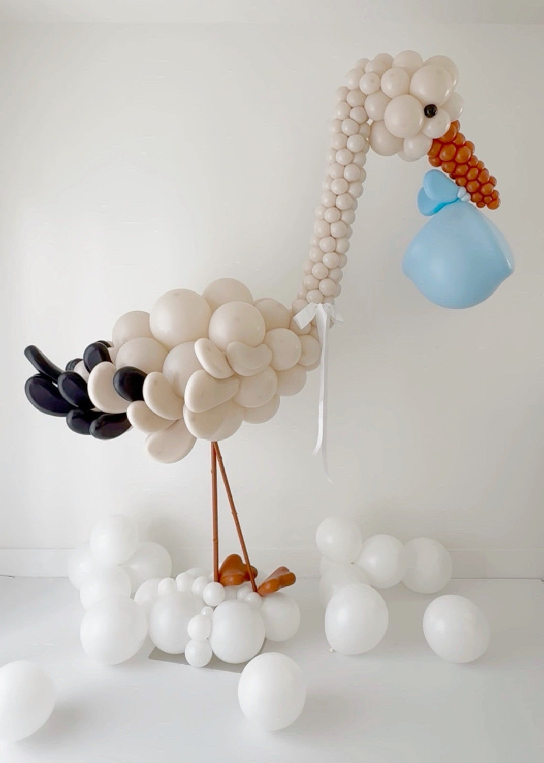 Elegant stork balloon design created with neutral balloons, standing on a cloud style base and holding a decorative balloon bundle, perfect for welcome baby displays, baby showers, and photography setups.