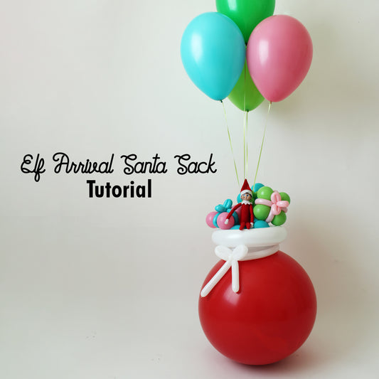 Whimsical Elf Arrival Santa Sack balloon decoration featuring a large red balloon base, tied with a white balloon bow and topped with an Elf on the Shelf, pastel presents, and floating helium balloons. This festive DIY project from Lilly Jimenez’s tutorial is perfect for Elf arrival ideas, holiday balloon décor, and creative Christmas setups.
