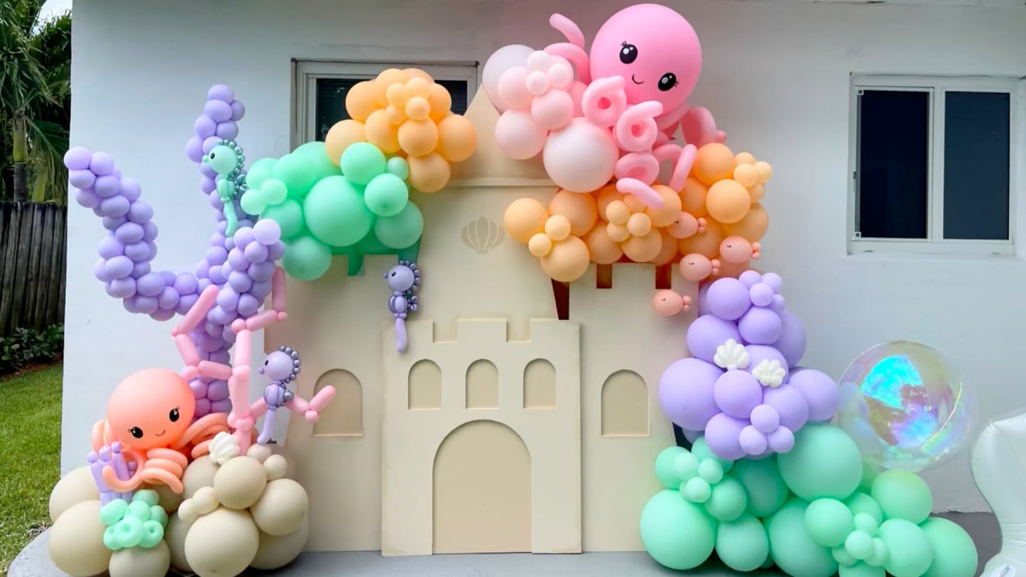 DIY Sand Castle Backdrop made from foam board, decorated with pastel balloon garlands featuring octopuses, sea horses, coral, and bubbles. This whimsical under-the-sea setup is part of Lilly Jimenez’s on-demand class from The Creative Heart Studio and is perfect for ocean, beach, princess, or storybook-themed parties.