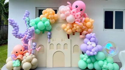 DIY Sand Castle Backdrop made from foam board, decorated with pastel balloon garlands featuring octopuses, sea horses, coral, and bubbles. This whimsical under-the-sea setup is part of Lilly Jimenez’s on-demand class from The Creative Heart Studio and is perfect for ocean, beach, princess, or storybook-themed parties.