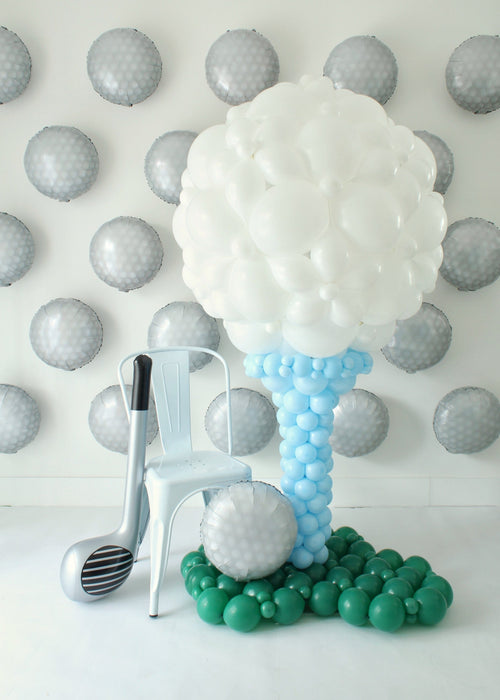 Golf Balloon Class setup featuring a giant balloon golf ball on a tee with a balloon golf club and golf ball prop beside a chair. This oversized balloon structure is part of the 2 video lessons and makes an eye-catching décor piece for golf tournaments, birthdays, baby showers, retirements, Father’s Day, corporate events, and store openings. A creative golf balloon décor idea that can also be customized with logos for branded celebrations.