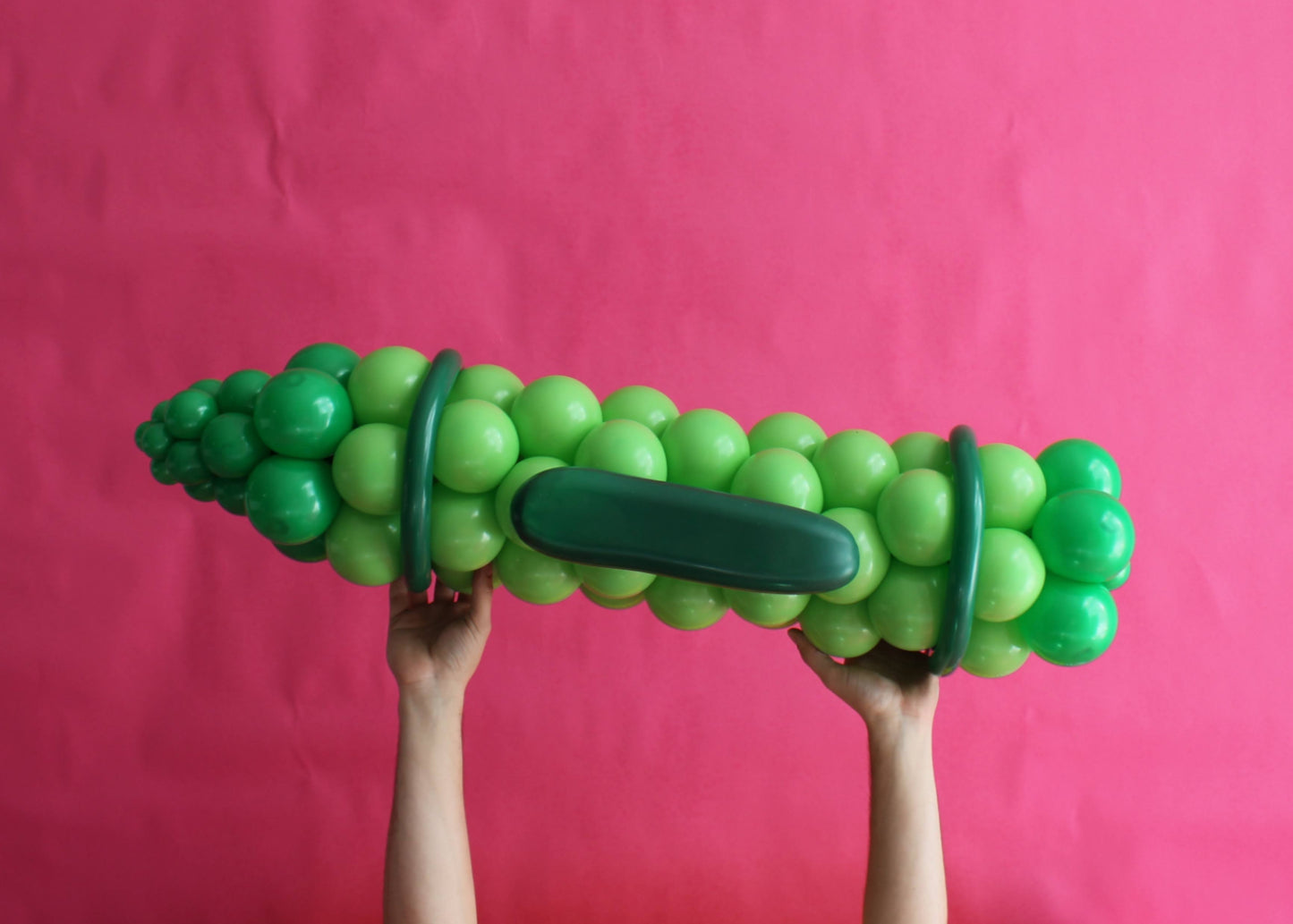 Oversized green balloon crayon prop held up against a pink backdrop. Made entirely of balloons in various shades of green, this back-to-school balloon sculpture is perfect for classroom displays, school photo ops, or educational-themed parties. Ideal for balloon artists looking to create bold, eye-catching decor with a school supplies theme.