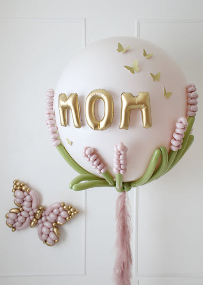 Elegant jumbo Mother's Day balloon featuring gold "MOM" letters, delicate pink balloon flowers, green stems, and butterfly accents. Perfect for gifting or party décor, this design adds a stunning touch to Mother’s Day celebrations.