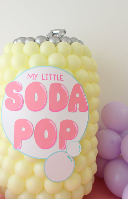 K-pop Demon Hunters themed soda pop balloon prop made with yellow balloons and topped with silver balloon details, featuring a large pink and white “My Little Soda Pop” label, perfect for themed parties, photo ops, and pastel K-pop inspired decor setups.