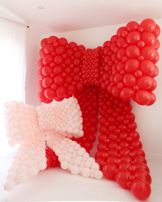 Red and pink balloon bow decorations on a white wall