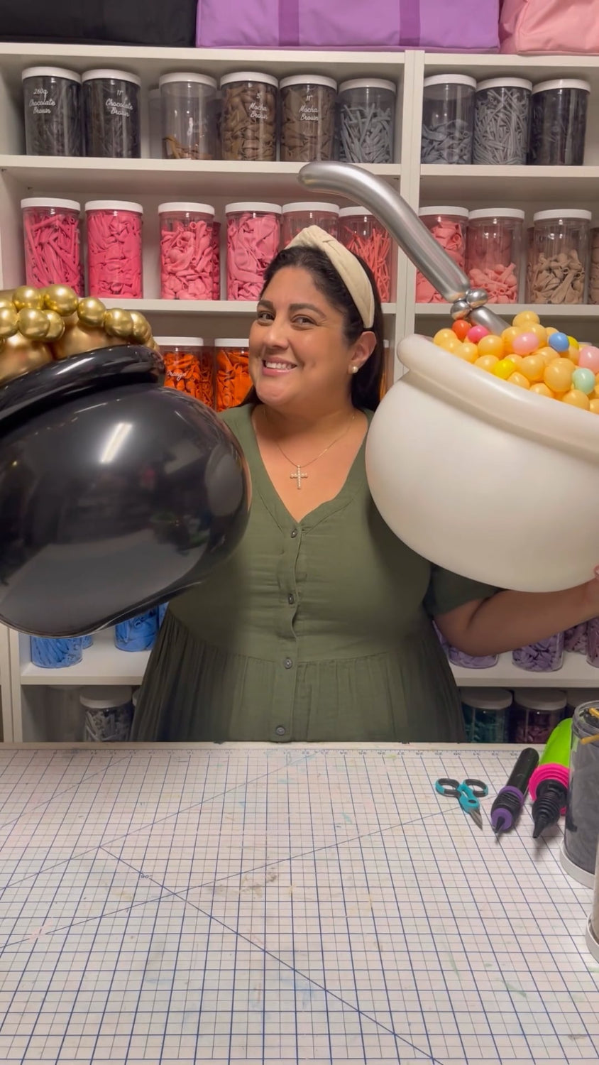 Lilly Jimenez, creator of the "You're My Lucky Charm Balloon Class," smiling and holding two balloon pots—one filled with gold balloons and the other with colorful cereal-style balloons and a silver spoon. A festive and fun behind-the-scenes look at the St. Patrick’s Day-themed balloon class. Perfect for holiday photo ops and party decor.