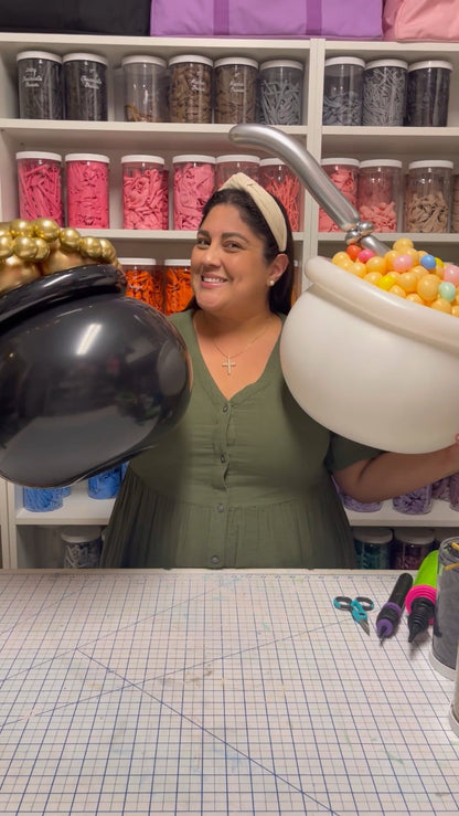 Lilly Jimenez, creator of the "You're My Lucky Charm Balloon Class," smiling and holding two balloon pots—one filled with gold balloons and the other with colorful cereal-style balloons and a silver spoon. A festive and fun behind-the-scenes look at the St. Patrick’s Day-themed balloon class. Perfect for holiday photo ops and party decor.