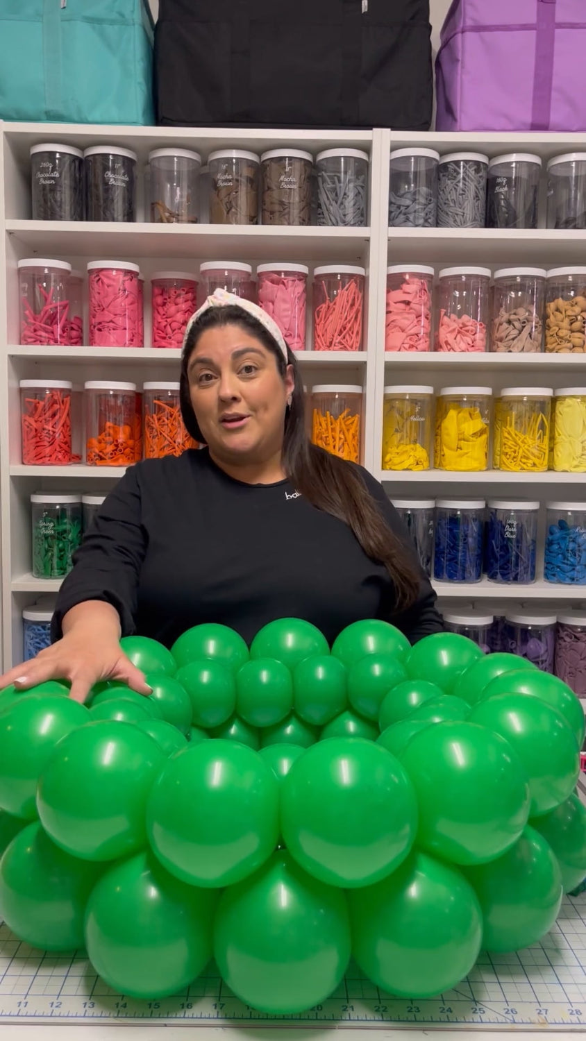 Lilly Jimenez demonstrates a festive green balloon wreath during her tutorial, surrounded by colorful supplies in her craft studio. This step-by-step holiday class is perfect for balloon artists and party decorators looking to create eye-catching seasonal wreaths without helium or framing.