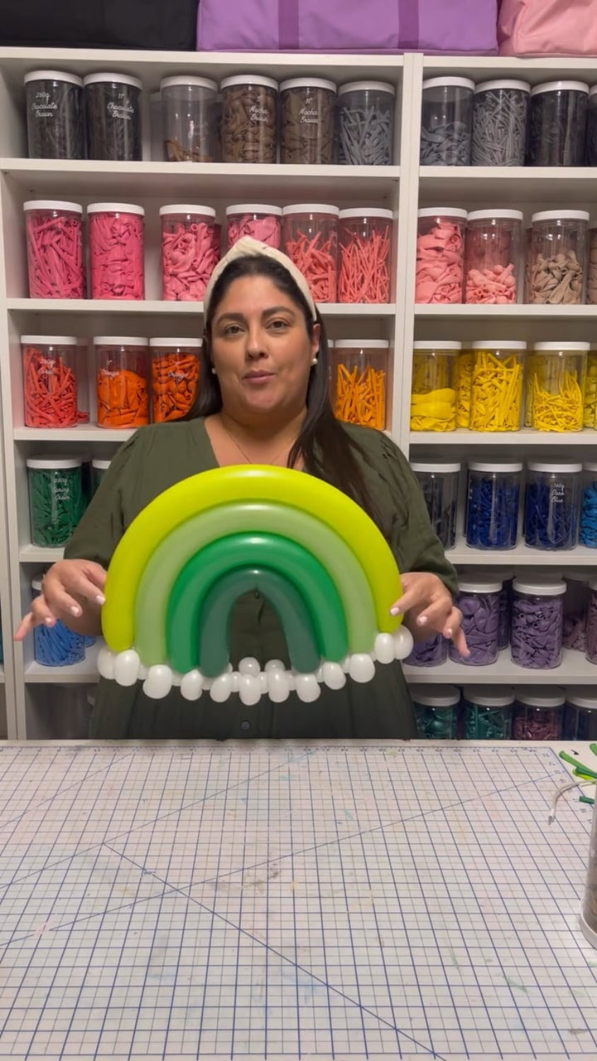 Lilly Jimenez holds a green monochrome balloon rainbow during her "You’re My Lucky Charm Balloon Class." Surrounded by colorful balloon jars, she demonstrates how to create this festive design for St. Patrick’s Day celebrations, party decor, or themed photoshoots.