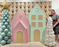 Festive holiday display featuring oversized pastel gingerbread houses in pink and mint green with candy-inspired trim, paired with balloon Christmas trees, including one topped with a gold star. Perfect for Christmas party decor, photo booths, and creative event styling.