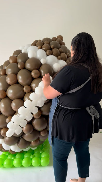 Lilly Jimenez assembling a massive football balloon sculpture made of brown, white, and green balloons. This oversized balloon design is perfect for Super Bowl parties, football-themed events, school spirit rallies, and sports banquets. The creative balloon installation highlights Lilly’s unique balloon artistry and makes a bold statement for any game day or sports celebration.