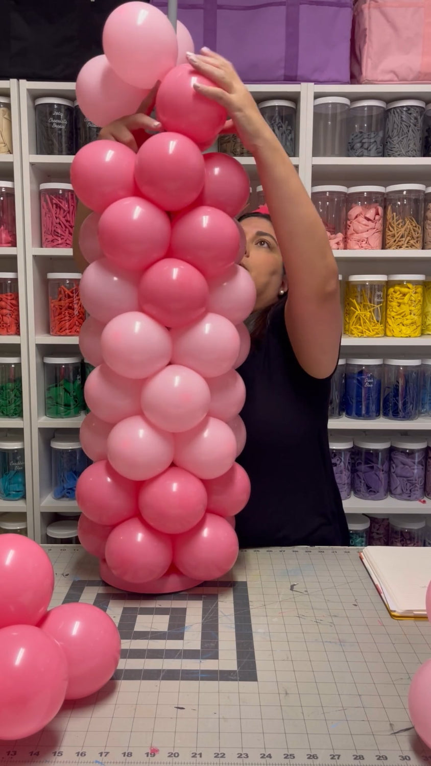 Lilly constructing a pink Balloon Crayon Column as part of the Back to School Column Class. This step-by-step balloon tutorial teaches how to build colorful school-themed balloon decor, including balloon pencil columns and crayon designs. The class includes video lessons and printable balloon recipes for balloon decorators and DIY event creators.