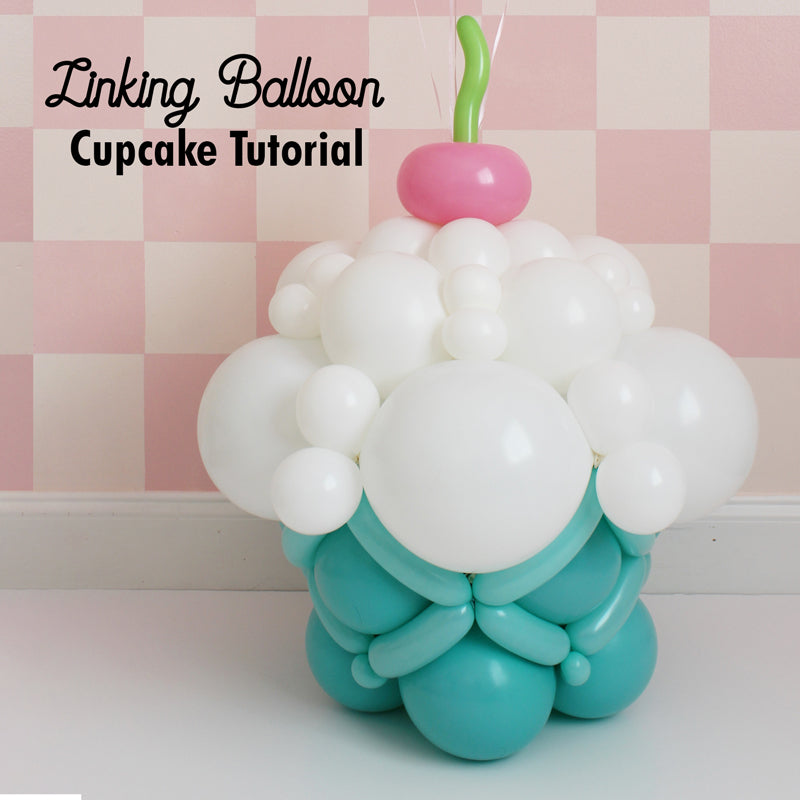 Oversized balloon cupcake made with linking balloons, featuring a teal base and white frosting topped with a pink balloon cherry and green swirl. This playful design is perfect for birthdays, candy-themed events, and balloon decor displays. Learn how to create it step-by-step in Lilly's Linking Balloon Cupcake Tutorial.
