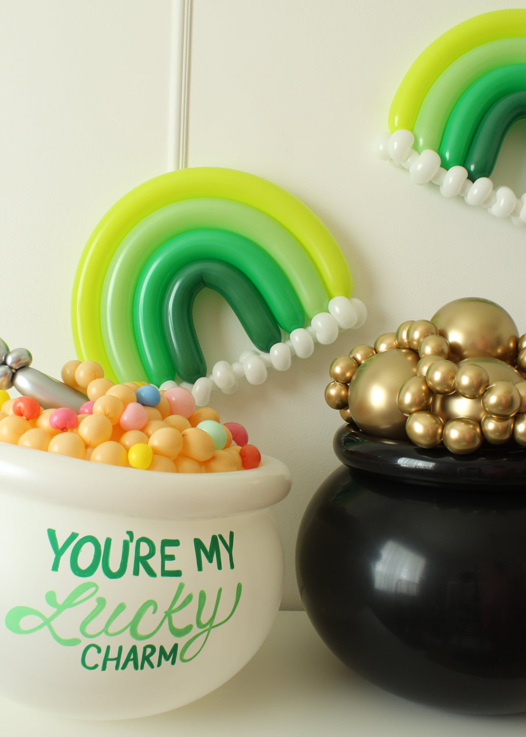 St. Patrick’s Day-themed balloon display featuring a monochrome green rainbow, a black pot of gold made with shiny gold balloons, and a white balloon cereal bowl labeled “You’re My Lucky Charm” filled with pastel balloon “cereal.” This setup is part of Lilly Jimenez’s You’re My Lucky Charm Balloon Class and is ideal for festive party decor and colorful photo backdrops.
