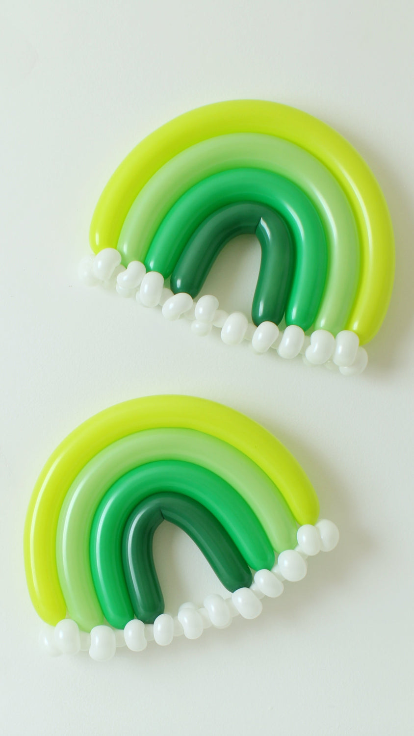 Pair of Lucky Monochrome Rainbow balloons in green and yellow shades with white balloon clouds, styled on a white wall. These festive balloon rainbows are part of the "You're My Lucky Charm Balloon Class" by Lilly Jimenez—perfect for St. Patrick’s Day parties, themed events, or colorful photo backdrops.