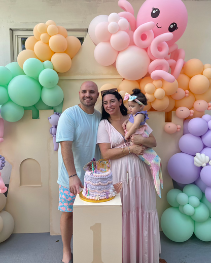 Mom and dad celebrate their daughter’s first birthday with a pastel balloon-decorated foam board Sand Castle Backdrop. The scene features a large pink balloon octopus, ocean-themed garlands, and a birthday cake on a “1” pedestal. This whimsical setup is part of the Sand Castle Backdrop Class by The Creative Heart Studio—perfect for beach, mermaid, or under-the-sea themed parties.
