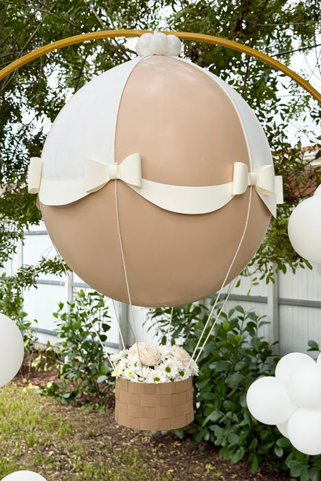Close-up of a Gender Reveal Hot Air Balloon featuring a beige and white jumbo balloon with decorative paper bows and a woven-style basket filled with white flowers, perfect for baby showers and gender reveal parties.