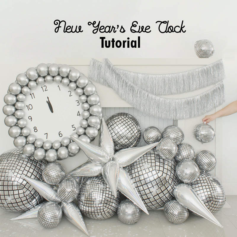 Glamorous New Year’s Eve balloon clock display featuring a large silver balloon clock with bold black hands pointing to midnight, surrounded by reflective disco ball balloons, metallic balloon stars, and silver fringe. Perfect for party decor or photo booth backdrops. Inspired by Lilly Jimenez’s tutorial for festive balloon installations and NYE celebration ideas.