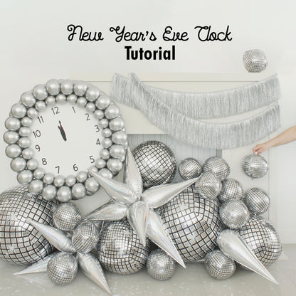 Glamorous New Year’s Eve balloon clock display featuring a large silver balloon clock with bold black hands pointing to midnight, surrounded by reflective disco ball balloons, metallic balloon stars, and silver fringe. Perfect for party decor or photo booth backdrops. Inspired by Lilly Jimenez’s tutorial for festive balloon installations and NYE celebration ideas.