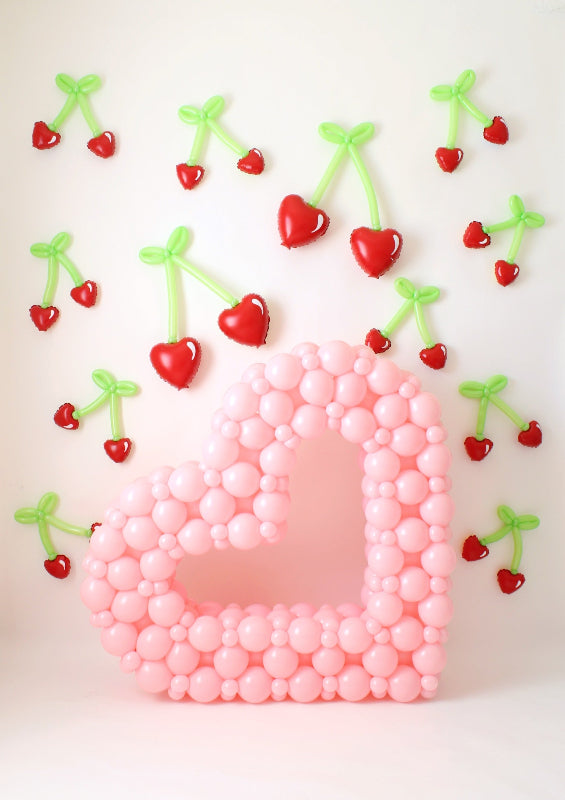 Pink open heart balloon sculpture surrounded by heart-shaped balloon cherries with green stems, creating a whimsical Valentine's display.