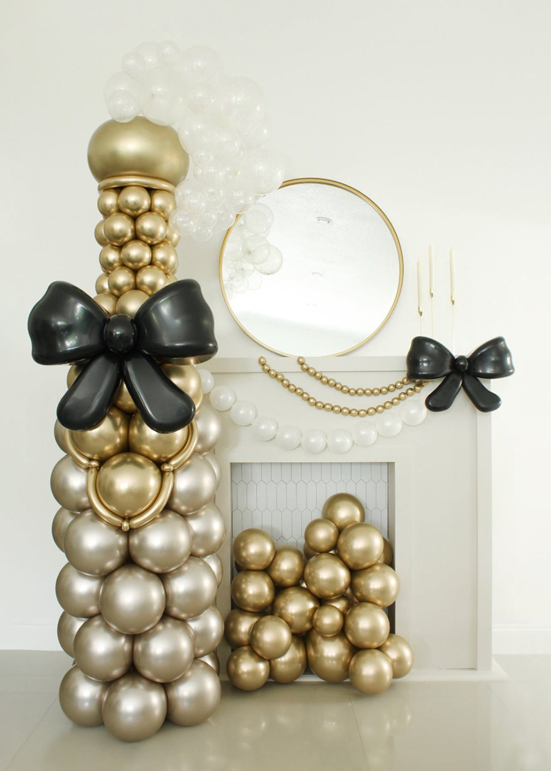 Stunning oversized balloon champagne bottle designed by Lilly Jimenez, decorated with metallic gold, pearl, and black balloons, topped with a statement balloon bow. Perfect for weddings, New Year’s Eve, and upscale party decor. The fireplace setup includes matching gold balloons and a coordinating black balloon bow—ideal for cocktail hour photo ops or elegant event backdrops.