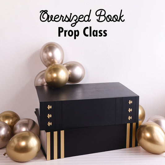 A black and gold oversized book prop designed for photoshoots, event decor, and themed celebrations. The sturdy, stacked book design allows people to sit on it for unique photo opportunities. Surrounded by gold and champagne balloons, this elegant prop is part of Lilly Jimenez’s Oversized Book Prop Class at The Creative Heart Studio. Perfect for graduations, back-to-school setups, and literary-themed events.