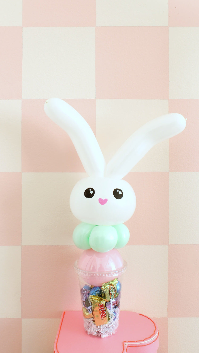 Easter-themed pastel bunny balloon candy cup with white balloon ears, mint green body, and cute face on top of a candy-filled cup. Perfect for spring gifts, Easter baskets, or party favors. Charming balloon art by Lilly adds a festive touch to Easter celebrations or candy displays.