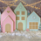Oversized pastel gingerbread village backdrop featuring three foam board houses in pink, mint, and blue with candy-style details, pearl wreaths, faux snow, string lights, and Christmas trees—perfect for festive photo sessions, holiday decor, or Christmas party displays.